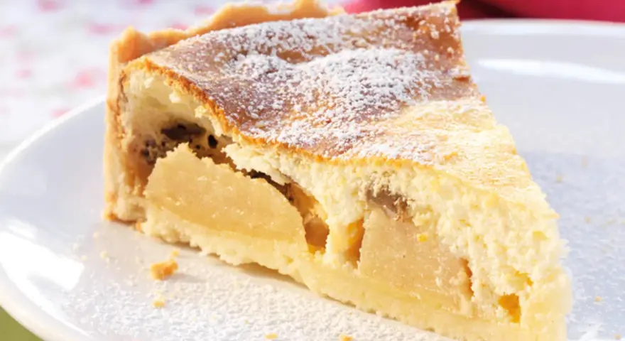 Ein Stück saftiger Apfelkuchen mit Quark, bestäubt mit Puderzucker, auf einem weißen Teller.