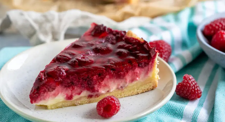 Ein saftiges Stück Himbeer Schmand Kuchen mit frischen Himbeeren und glänzender Glasur auf einem Teller.
