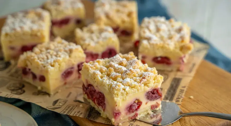 Saftiger Kirschkuchen mit Pudding und Streuseln, bestäubt mit Puderzucker. Ein Stück wird gerade serviert.