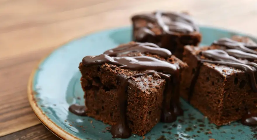 Saftige Brownies, perfekt für ein schnelles Brownie Rezept. Mit flüssiger Schokolade übergossen und auf einem türkisfarbenen Teller angerichtet.