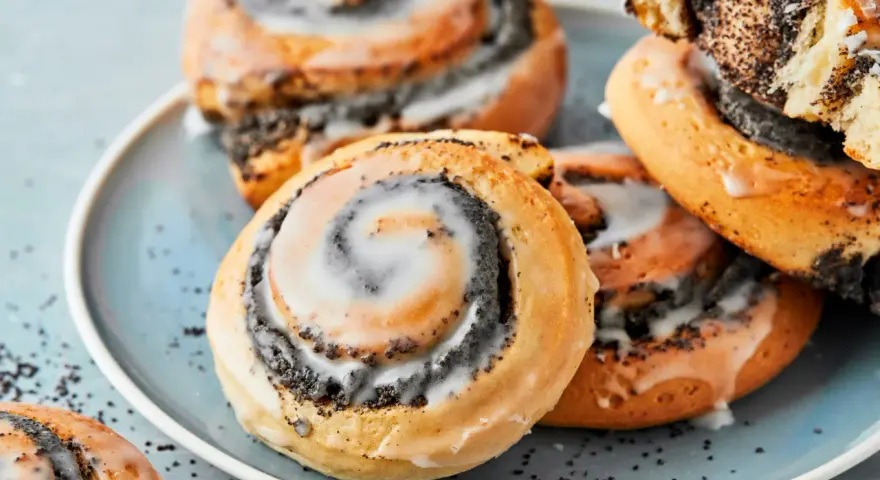 Saftige Mohnschnecken mit Zuckerguss auf einem blauen Teller. Dieses Bild inspiriert zum Nachbacken mit einem einfachen Mohnschnecken Rezept.