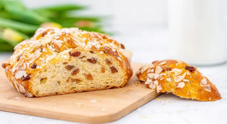 Ein goldbraunes Osterbrot mit Mandelsplittern und Rosinen, perfekt für Ihr Osterbrot Rezept. Daneben ein Stück des süßen Gebäcks.