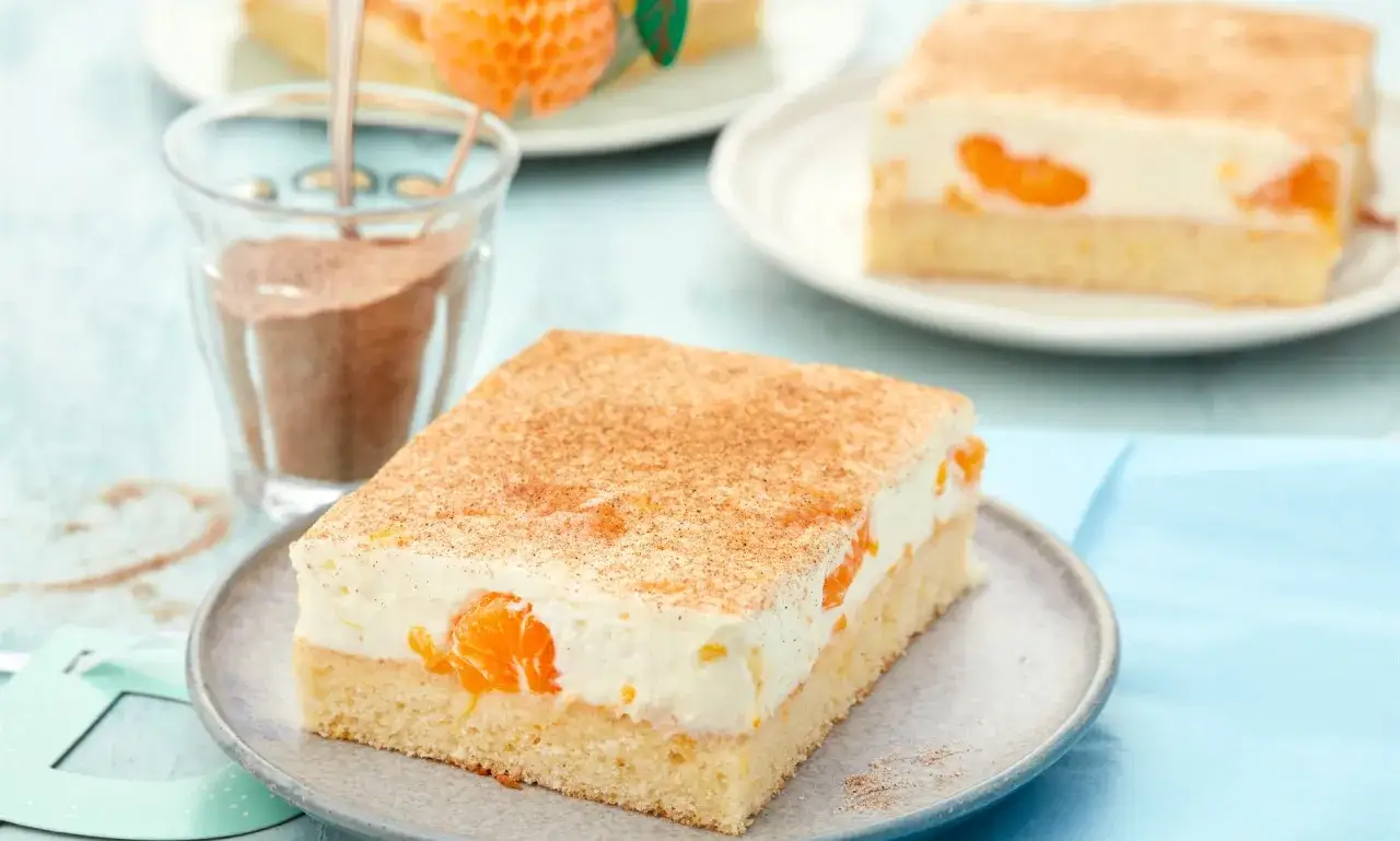 Ein Stück saftiger faule weiber kuchen mit Mandarinen und Zimt bestreut. Daneben ein Glas mit Zimt.