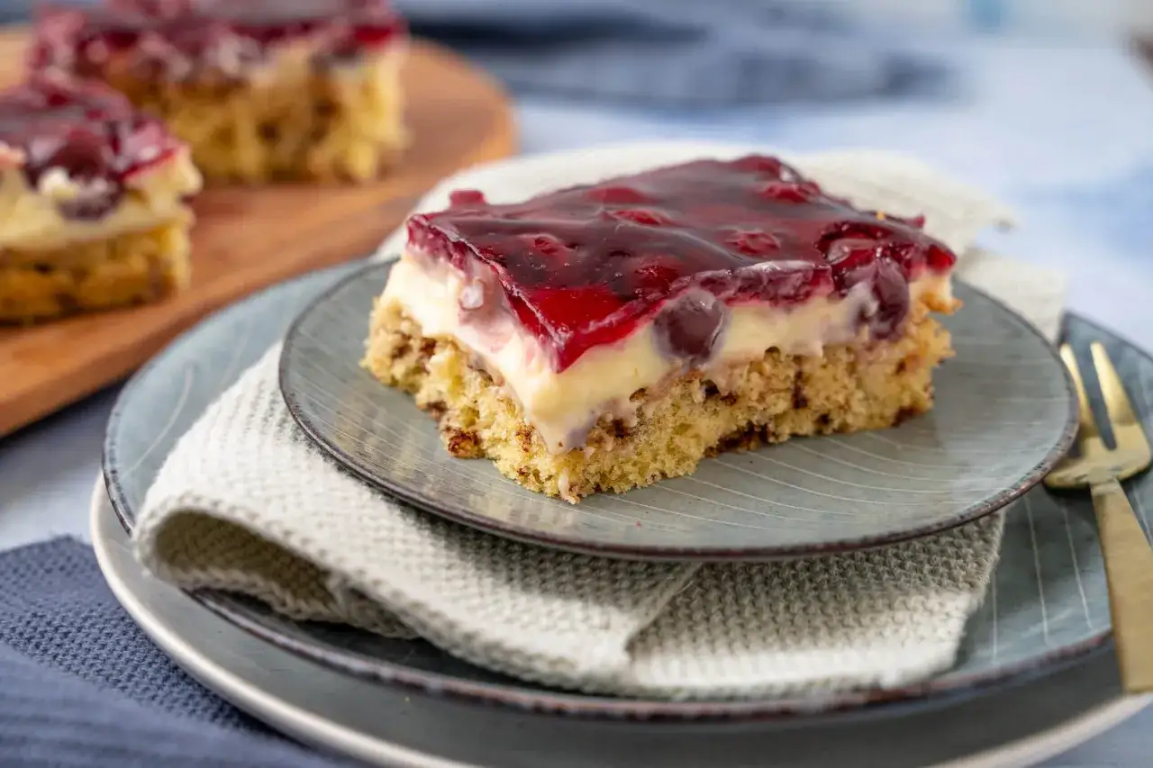 Ein saftiges St&uuml;ck kirschkuchen mit pudding und Kirschen, bedeckt mit rotem Gelee.