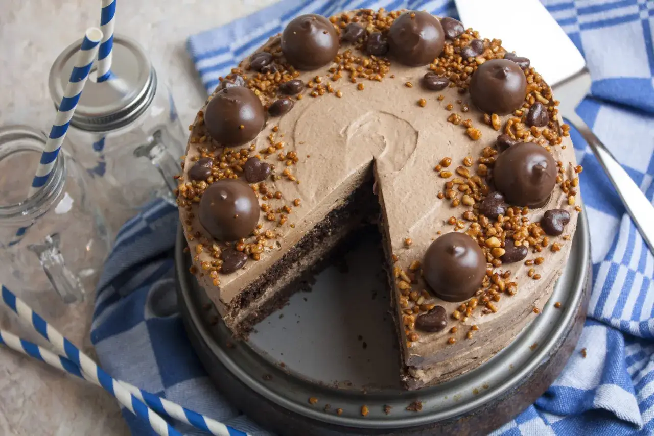 Schokoladige nougat torte mit Nüssen und Pralinen, bereit zum Servieren mit blauen Strohhalmen.