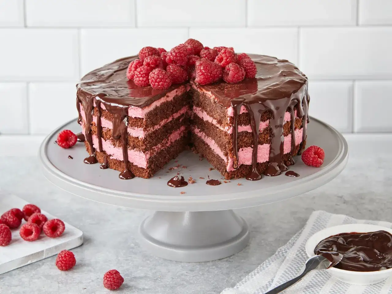 Schokoladen-Himbeer-Torte mit rosa Füllung, ein perfektes Rezept für Valentinstag. Frische Himbeeren krönen den Schokoladenguss.