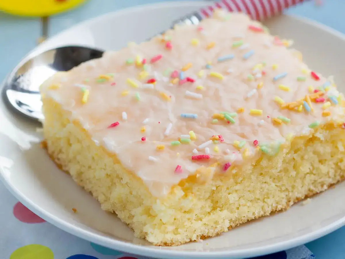 Ein St&uuml;ck saftiger Fantakuchen mit Zuckerguss und bunten Streuseln, perfekt f&uuml;r das Fantakuchen Rezept.