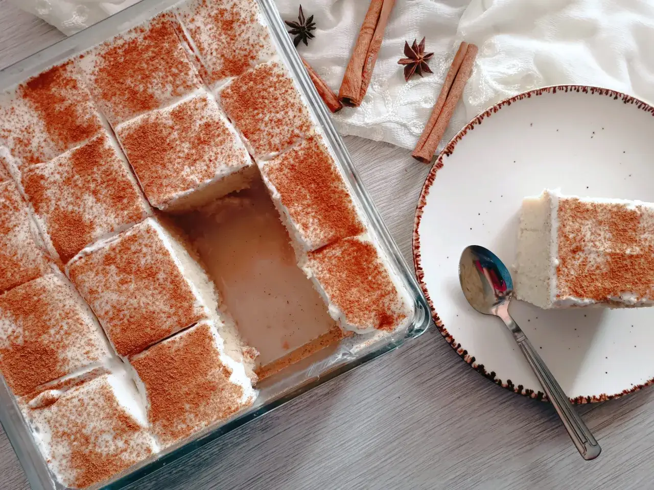 Saftiger Kuchen, bestreut mit Zimt, liegt in einer Glasform. Ein St&uuml;ck Tres Leches auf einem Teller daneben l&auml;dt zum Genuss ein.