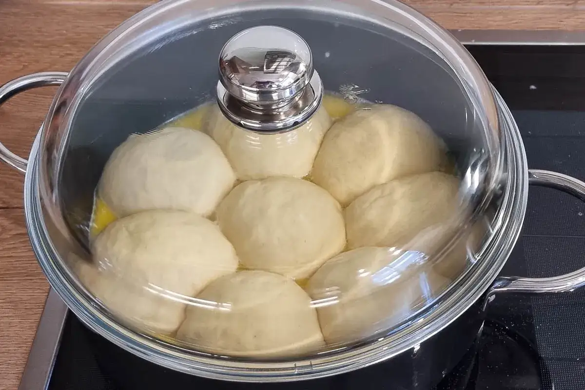Dampfnudeln rezept: Teiglinge garen in einem Topf unter einem Glasdeckel.
