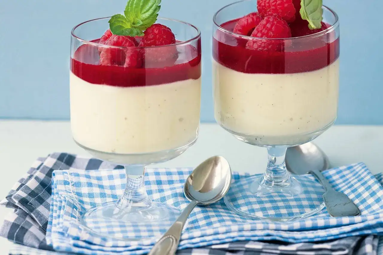 Zwei Gläser mit cremiger bayrischer Creme, garniert mit Himbeeren und Minze, auf karierter Serviette.