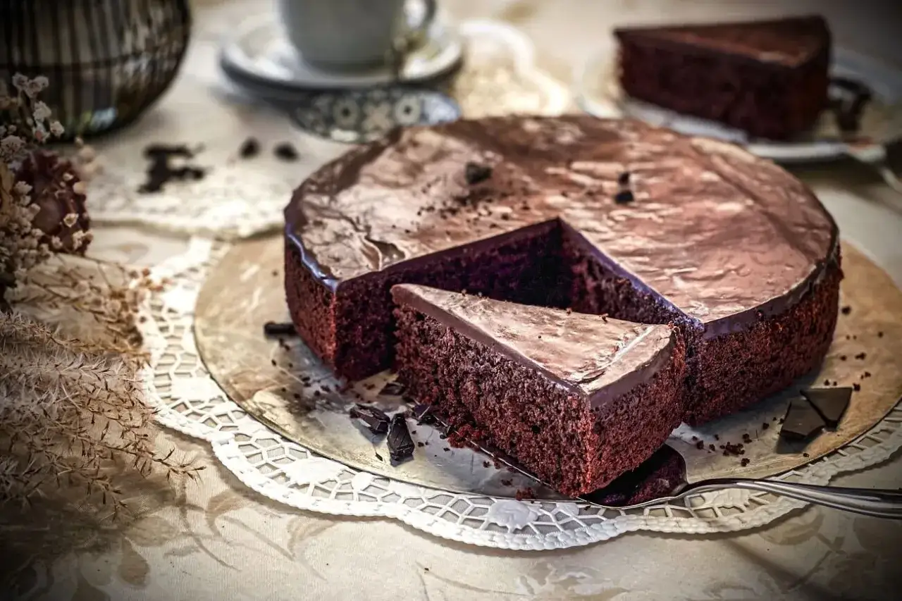 Ein saftiger, schneller Schokokuchen mit glänzender Glasur und einer Kuchenscheibe, die gerade herausgeschnitten wird.