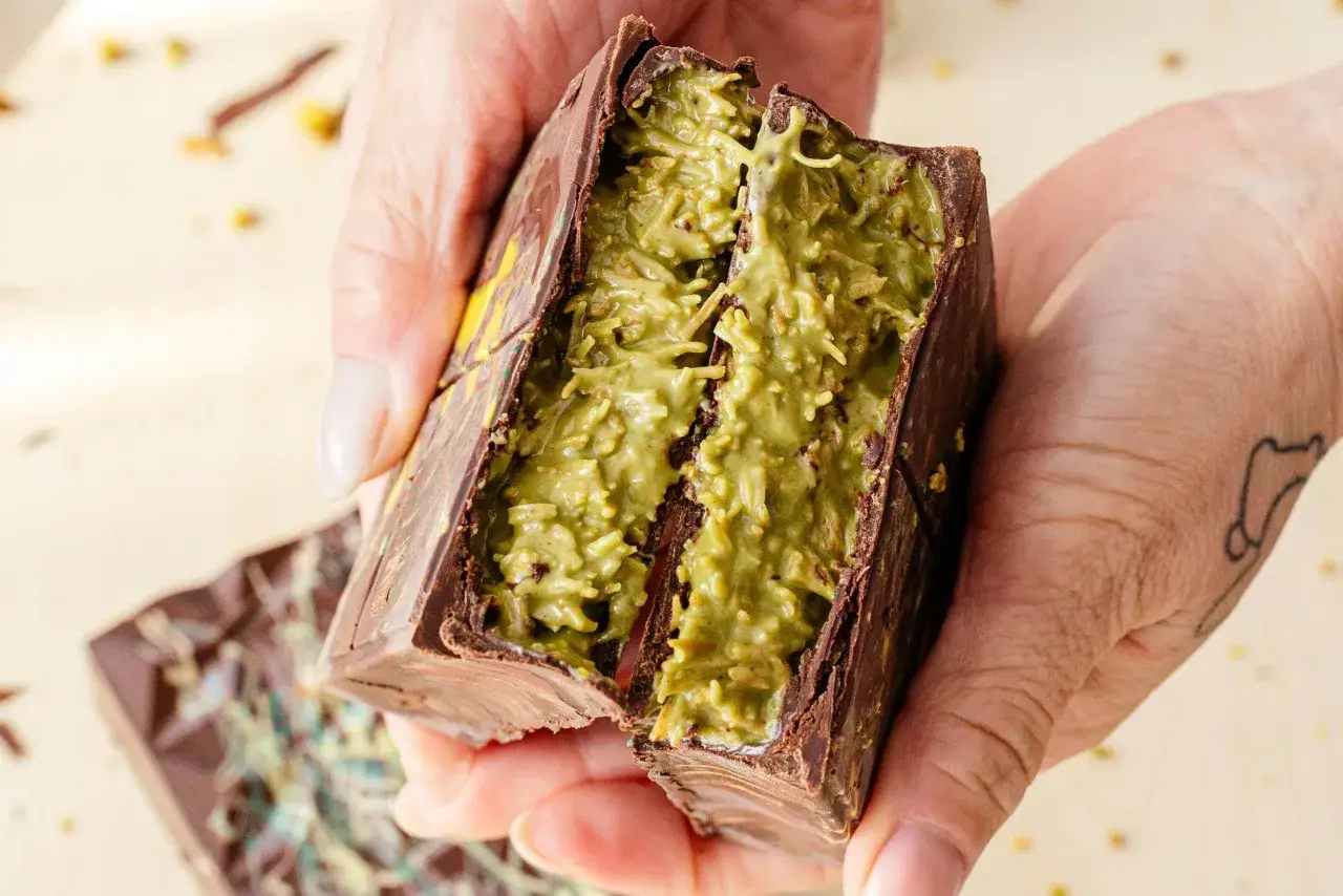 H&auml;nde halten eine aufgeschnittene Schokoladentafel mit gr&uuml;ner Pistazienf&uuml;llung. Ein k&ouml;stliches Dubai Schokolade Rezept zum Nachmachen.