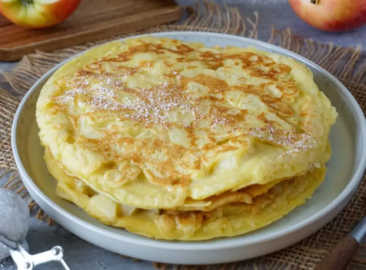 Ein Stapel goldbrauner Apfelpfannkuchen, bestäubt mit Puderzucker. Dieses Apfelpfannkuchen Rezept ist ein Genuss!