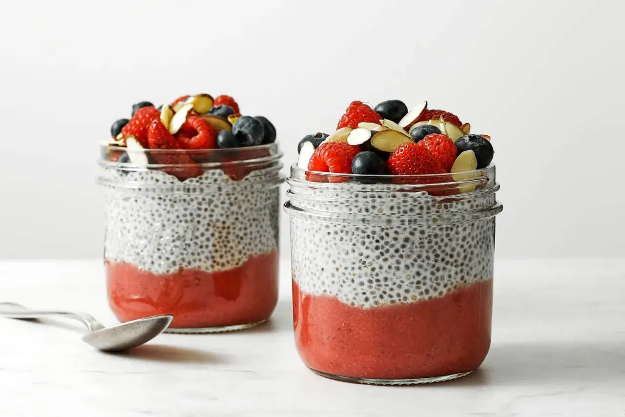 Zwei Gl&auml;ser Chia Pudding mit Erdbeerp&uuml;ree und frischen Beeren, garniert mit Mandelsplittern. Ein L&ouml;ffel liegt daneben.
