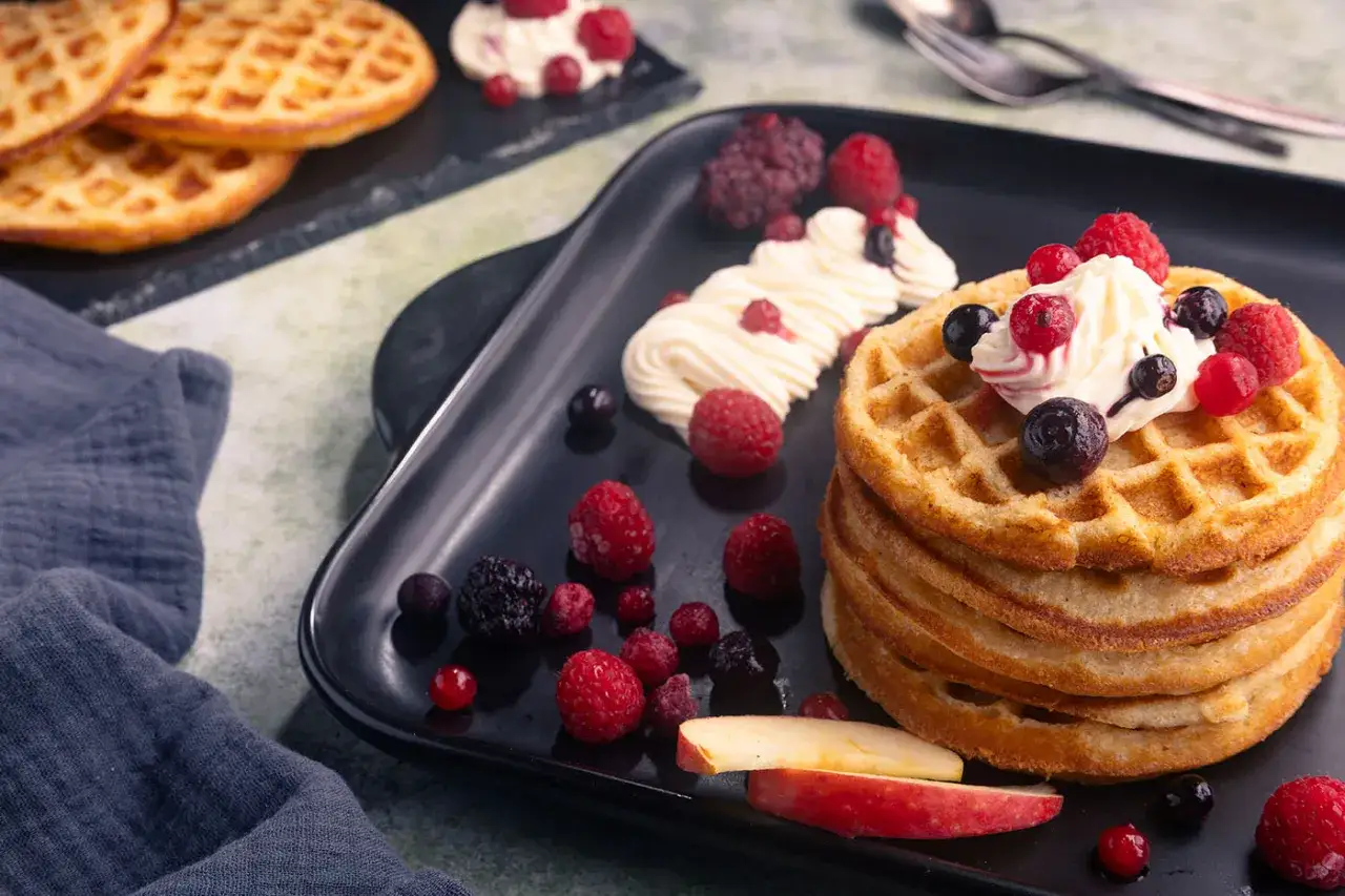 Ein Stapel goldbrauner Waffeln, garniert mit Sahne und Beeren, perfekt für ein Apfelwaffeln Rezept.