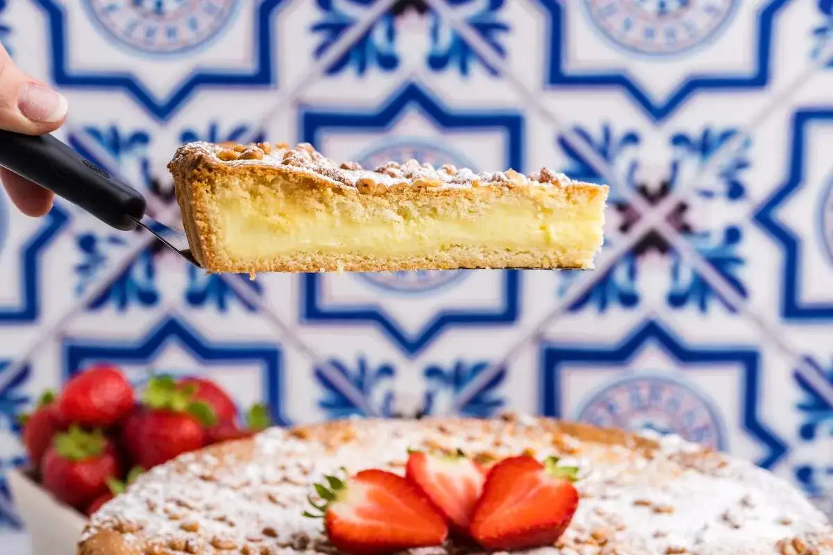 Ein St&uuml;ck Torta della Nonna mit cremiger F&uuml;llung wird serviert. Frische Erdbeeren und Puderzucker zieren den Kuchen.