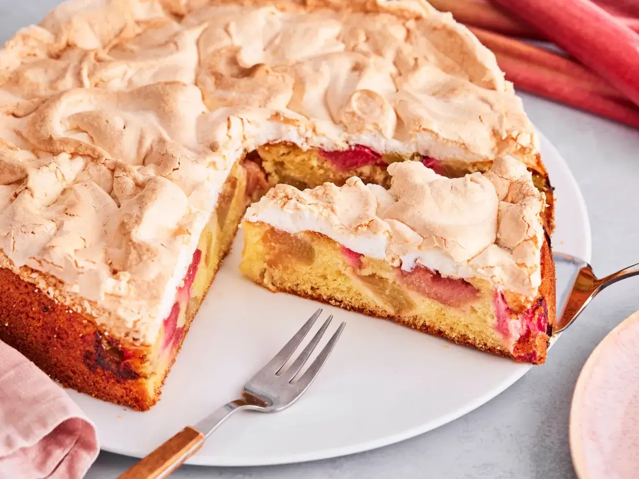 Saftiger Rhabarberkuchen mit luftigem Baiser, ein Stück wird gerade serviert.