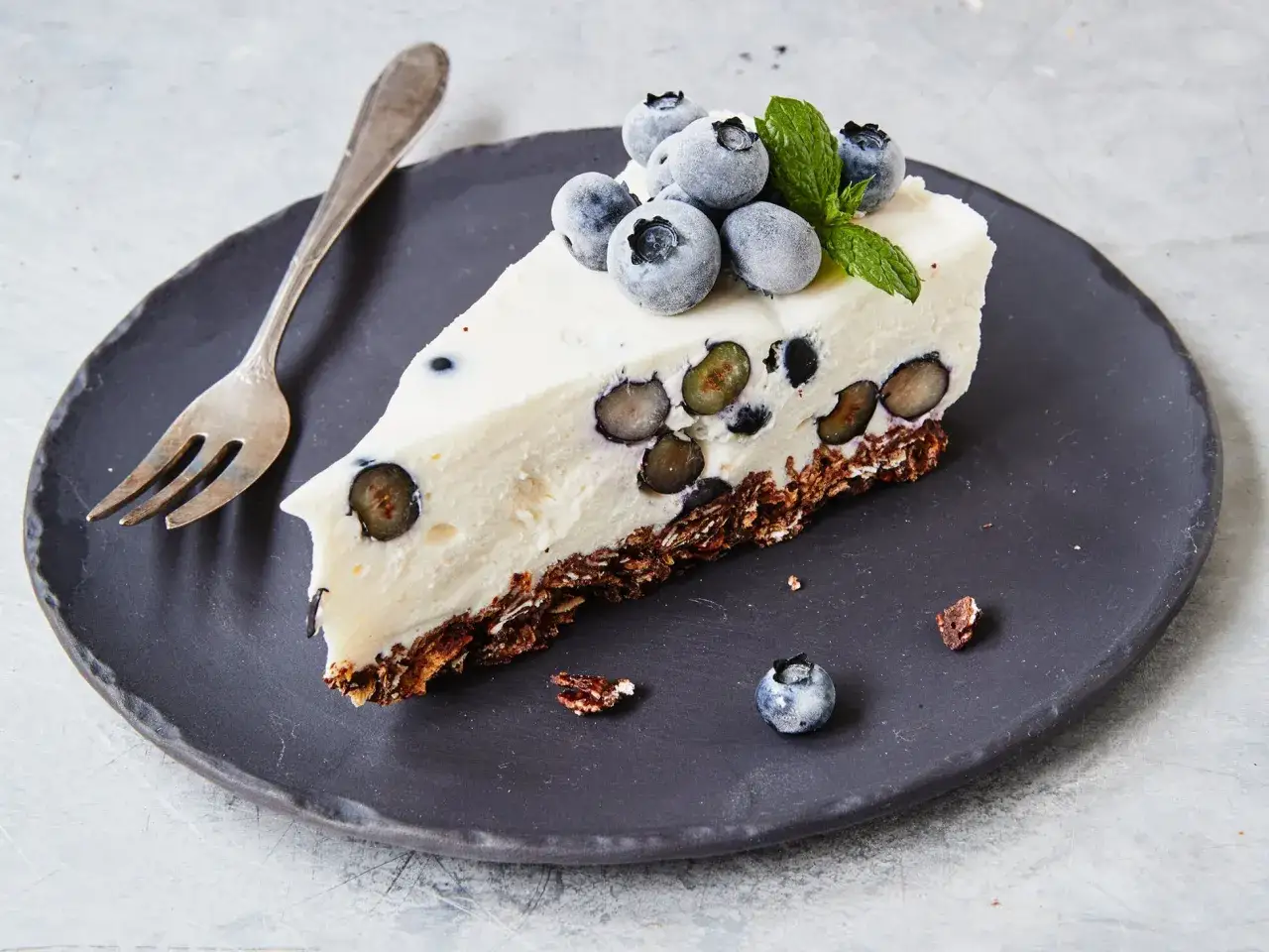 Ein Stück cremiger Kuchen mit Mascarpone und Blaubeeren, garniert mit frischen Beeren und Minze.