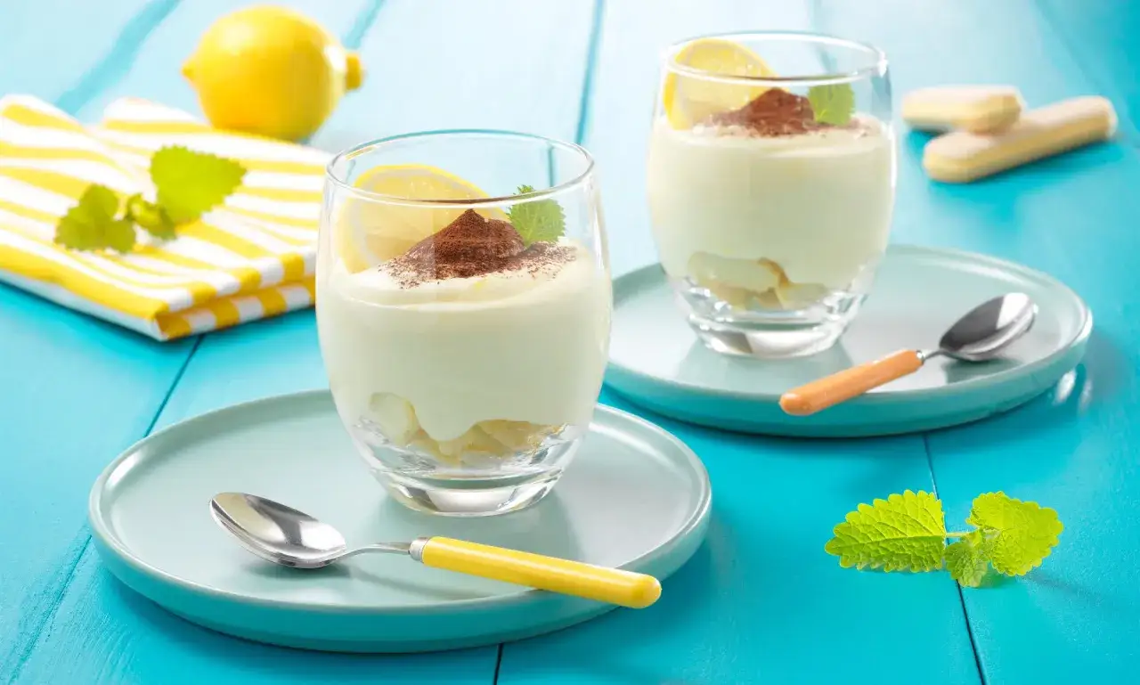 Zwei Gl&auml;ser mit cremigem Zitronen Tiramisu, garniert mit Kakaopulver und Zitronenscheiben. Ein erfrischender Genuss!