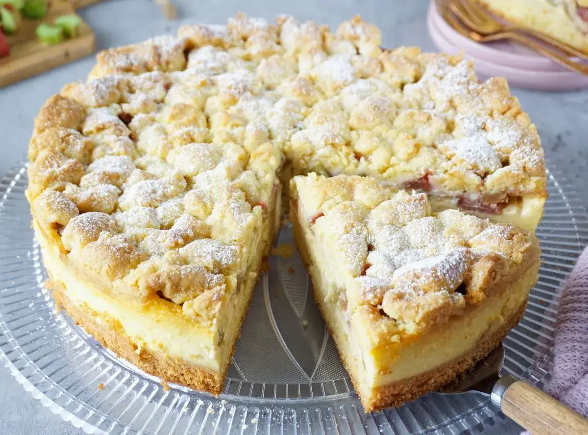 Saftiger Rhabarber-Streuselkuchen, perfekt für Rhabarber Rezepte. Mit cremiger Füllung und knusprigen Streuseln, bestäubt mit Puderzucker.
