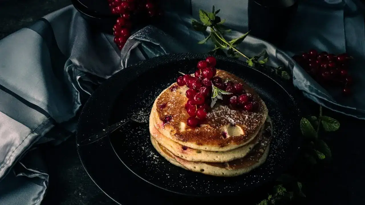 Ein Stapel goldbrauner Pancakes, garniert mit roten Johannisbeeren und Puderzucker. Perfekt für ein leckeres Pancakes Rezept.