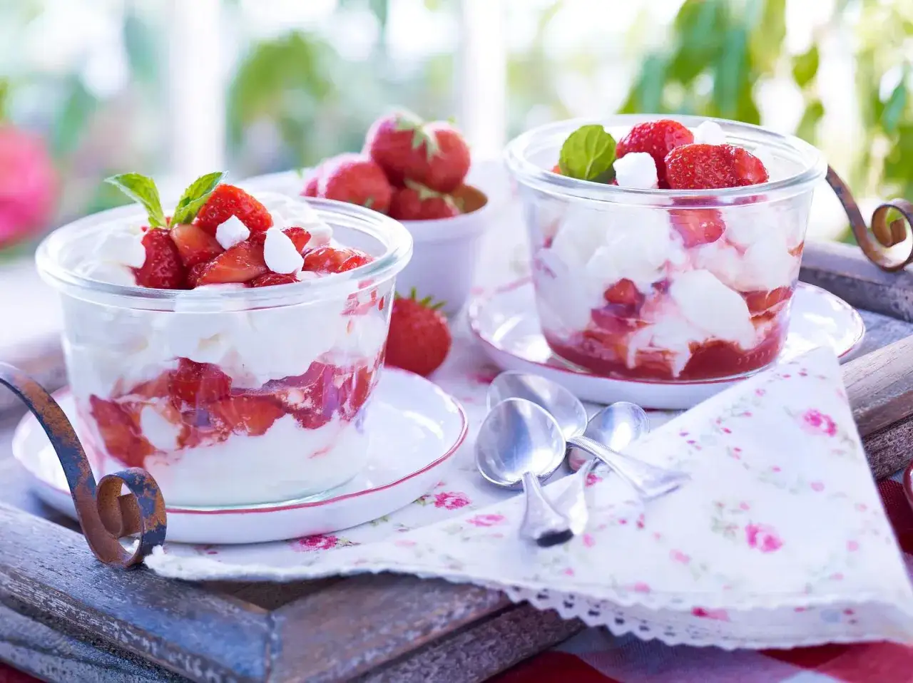 Zwei Gläser mit Eton Mess, geschichtet aus Sahne, zerbrochenem Baiser und frischen Erdbeeren, garniert mit Minze.