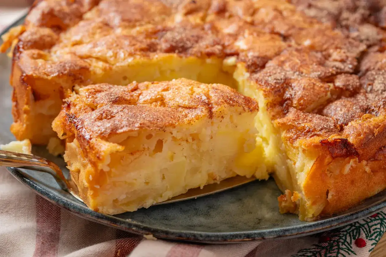 Ein Stück saftiger Apfelkuchen mit goldbrauner Kruste wird mit einem Tortenheber herausgehoben.
