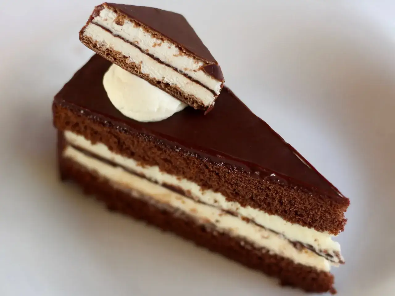 Ein Stück Schokoladenkuchen mit weißer Creme und Schokoladenglasur, wie eine Kinder Pingui Torte.