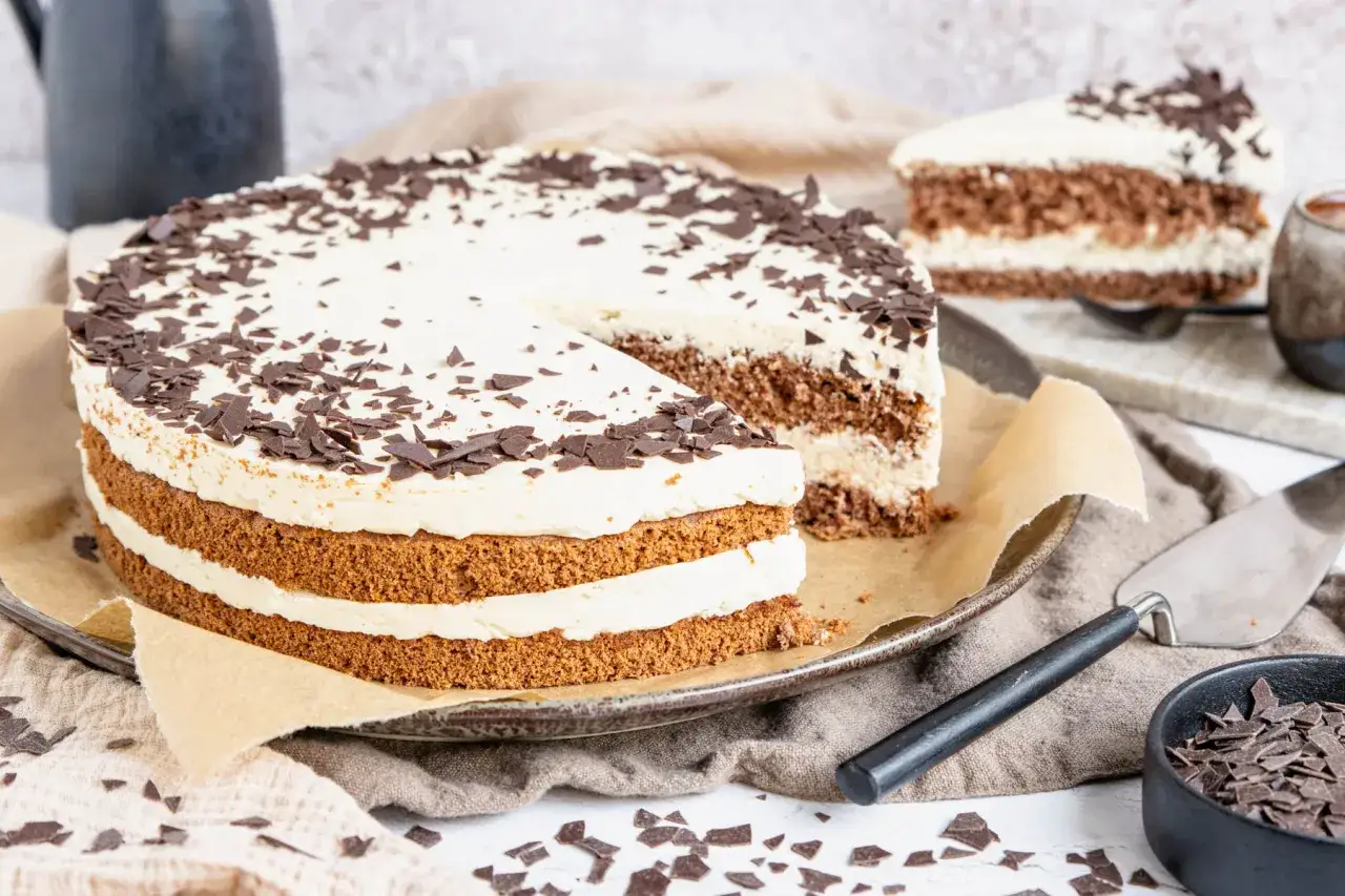 Eine köstliche Cappuccino Torte mit Schokoladenraspeln, auf einem Teller mit einem angeschnittenen Stück.