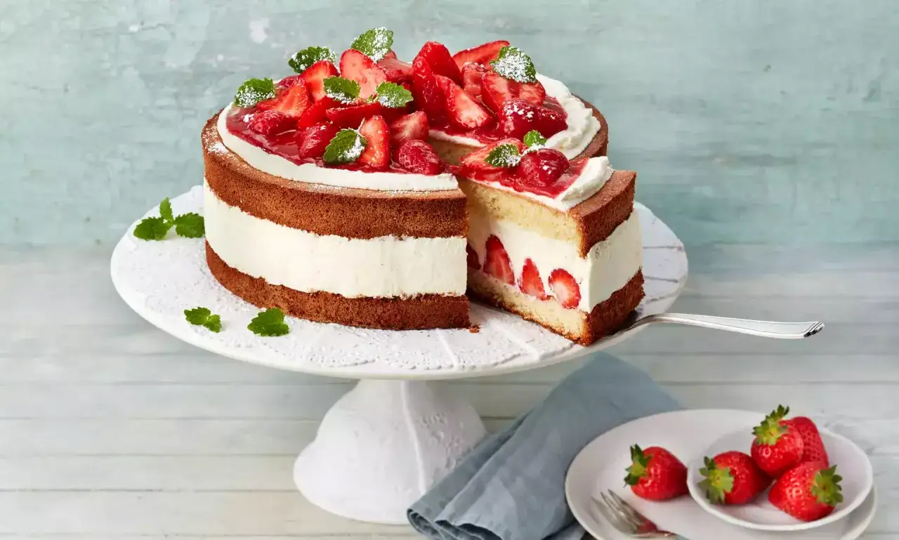 Saftige Erdbeer-Sahne-Torte mit frischen Erdbeeren und Minze, ein St&uuml;ck wurde bereits entnommen.