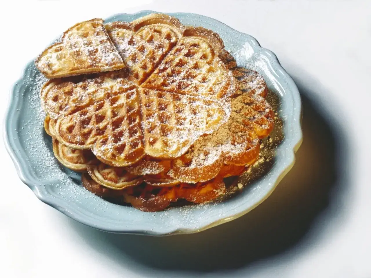 Herzförmige Waffeln, bestäubt mit Puderzucker, auf einem blauen Teller. Ein köstlicher waffelteig ohne butter.