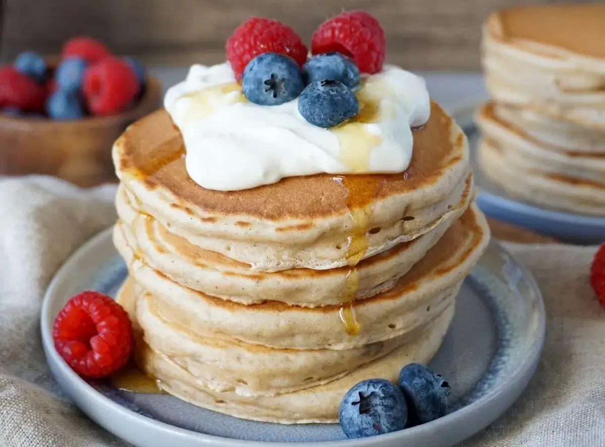 Ein Stapel fluffiger Bananen Pancakes, garniert mit Sahne, Beeren und Honig. Ein köstlicher Start in den Tag!