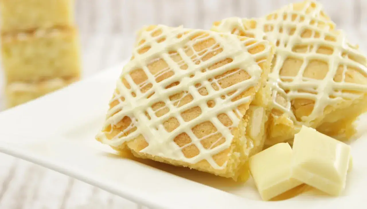 Zwei goldbraune Blondies mit weißer Schokoladenglasur und Schokostückchen. Ein köstliches Blondies Rezept zum Nachbacken.