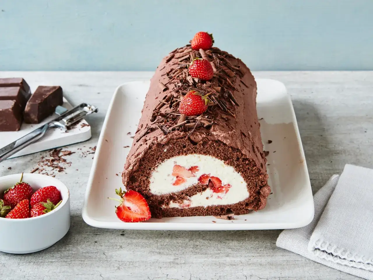Schoko Biskuitrolle mit Erdbeerfüllung, dekoriert mit Schokostreuseln und frischen Erdbeeren.
