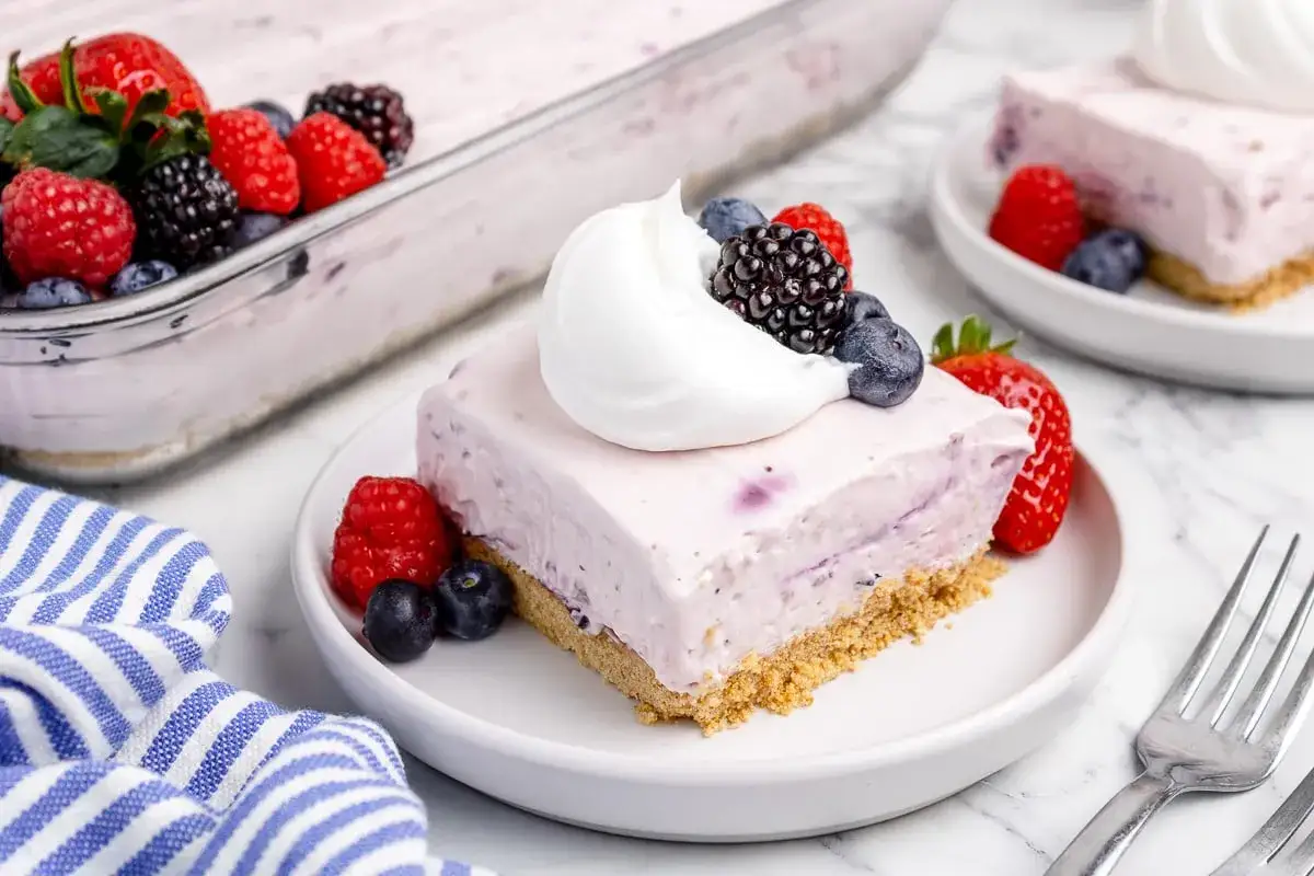 Ein Stück cremiges No-Bake Cheesecake mit Beeren und Sahne. Perfekt für heiße Tage!