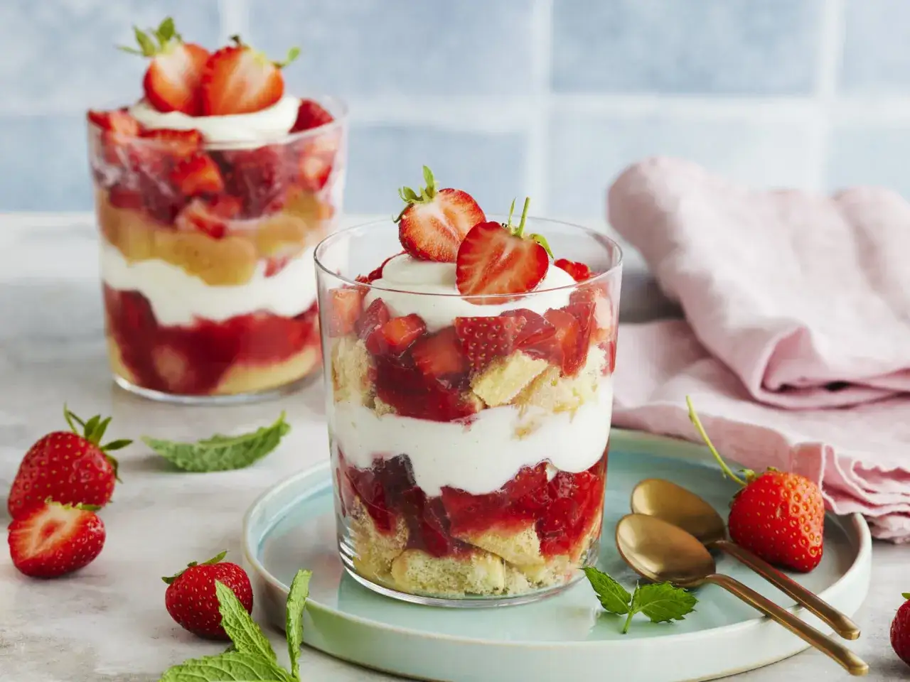 Zwei Gl&auml;ser mit Erdbeer Tiramisu, geschichtet mit Biskuit, Sahne und frischen Erdbeeren, garniert mit Erdbeeren und Minze.
