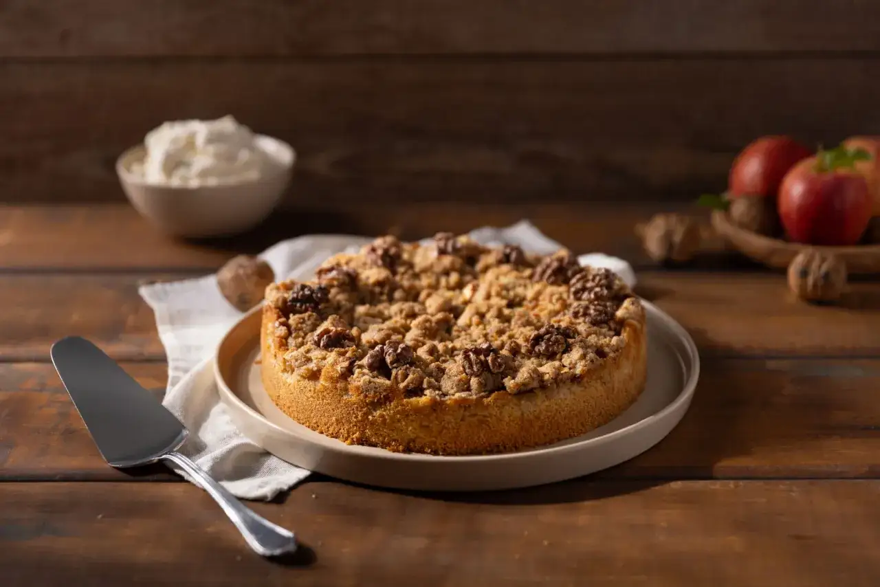 Ein köstlicher Apfelkuchen mit Streuseln und Walnüssen, bereit zum Servieren. Daneben eine Schüssel mit Sahne und Äpfel.