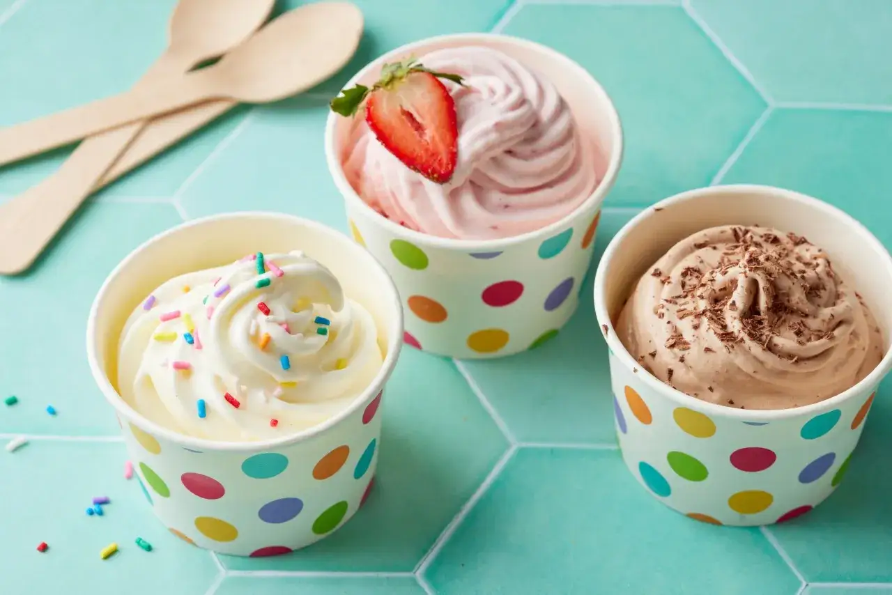 Drei Becher mit leckerem frozen joghurt: Vanille mit Streuseln, Erdbeer-Joghurt mit Erdbeere und Schoko-Joghurt mit Schokostreuseln.