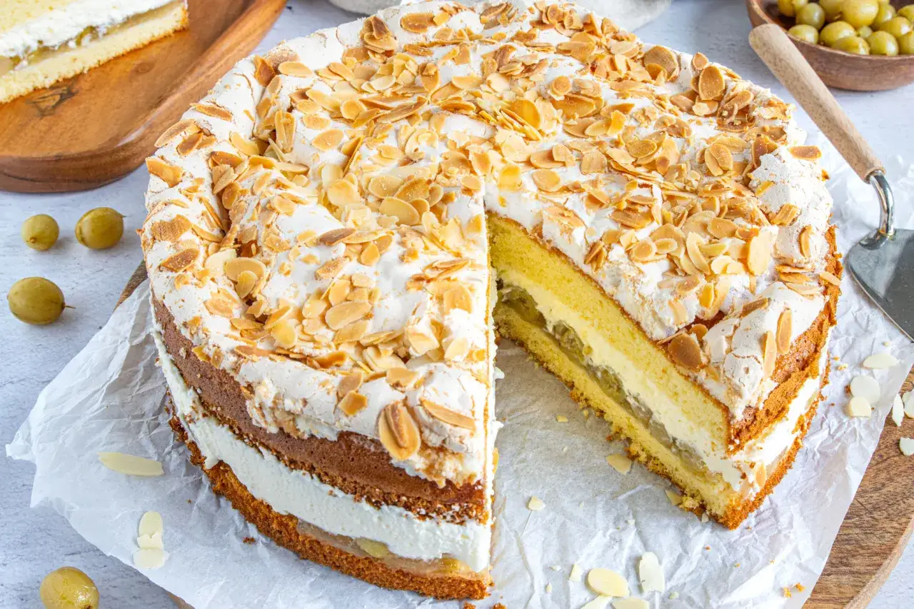 Eine köstliche Stachelbeer Baiser Torte mit Mandelsplittern und einer cremigen Füllung. Ein Stück ist bereits angeschnitten.