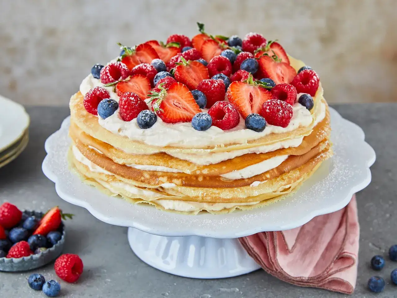 Eine üppige Pfannkuchen Torte, geschichtet mit Sahne und garniert mit frischen Erdbeeren, Himbeeren und Blaubeeren.