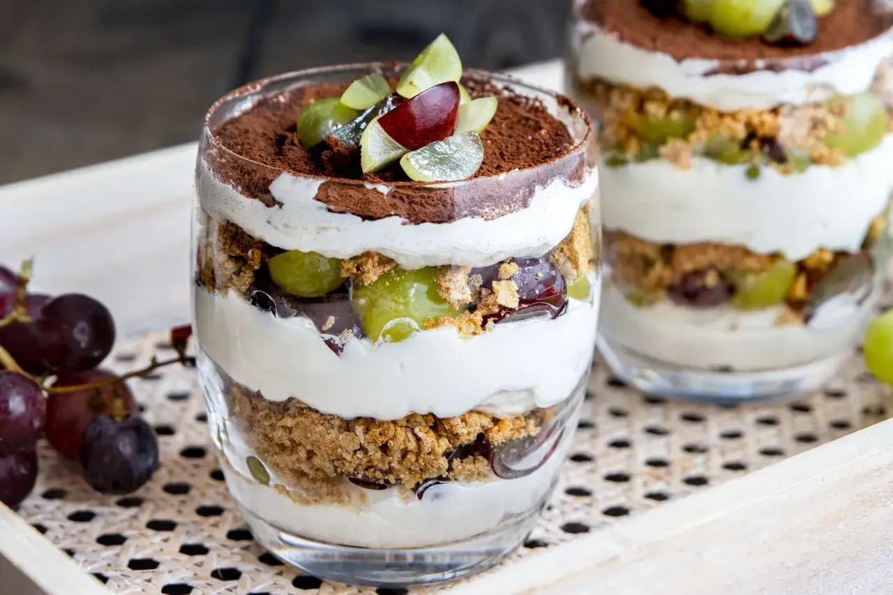 Schichtdessert im Glas mit cremigem Frischkäse, zerbröselten Keksen, saftigen Trauben und Kakaopulver. Ein köstliches Trauben Cookie Dessert.