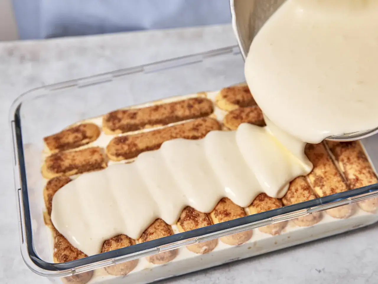 Cremige Masse wird über Löffelbiskuits gegossen, ein Schritt im tiramisu rezept.
