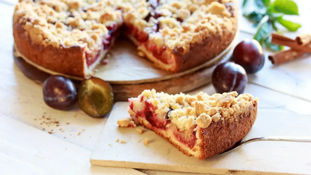 Ein saftiger Zwetschgenkuchen mit knusprigem Streusel-Topping, perfekt für jedes Streusel Rezept. Daneben liegen frische Zwetschgen und Zimtstangen.