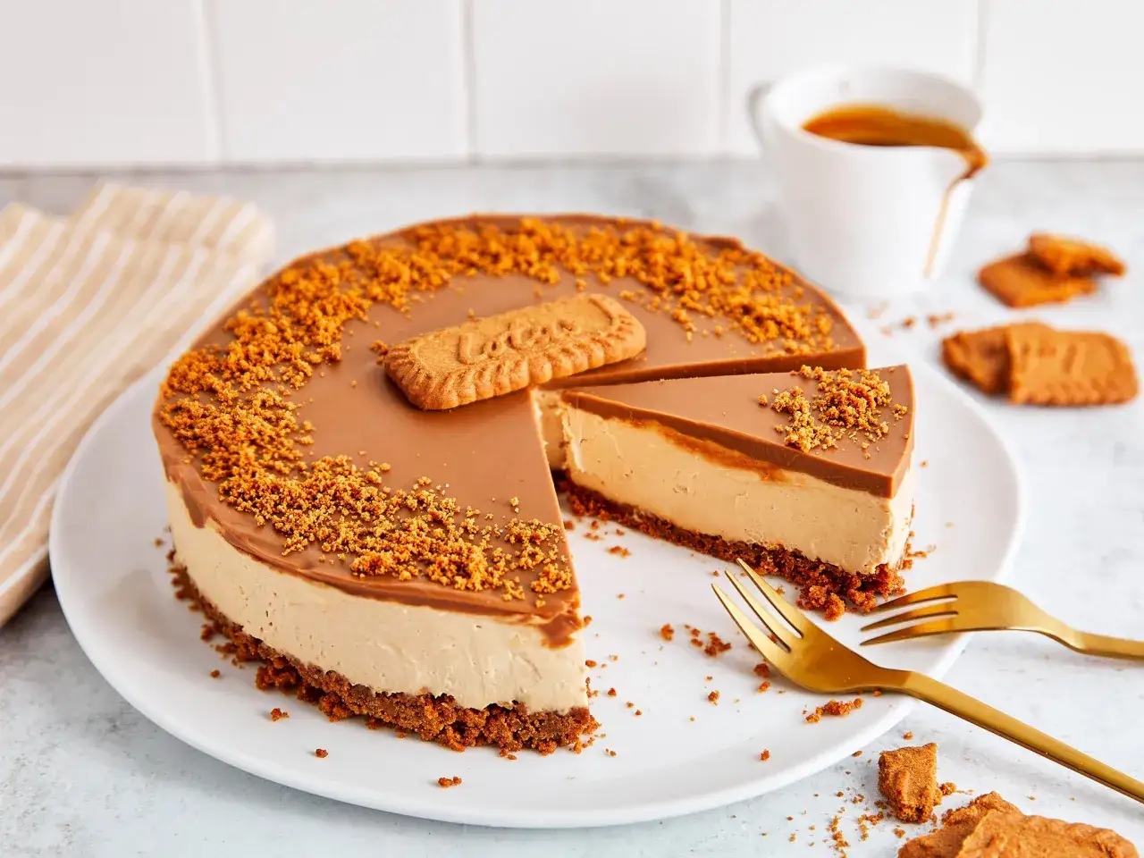 Ein köstlicher Lotus Cheesecake mit Karamellglasur und Keksbröseln, garniert mit einem Lotus Keks. Dazu eine Tasse Kaffee.