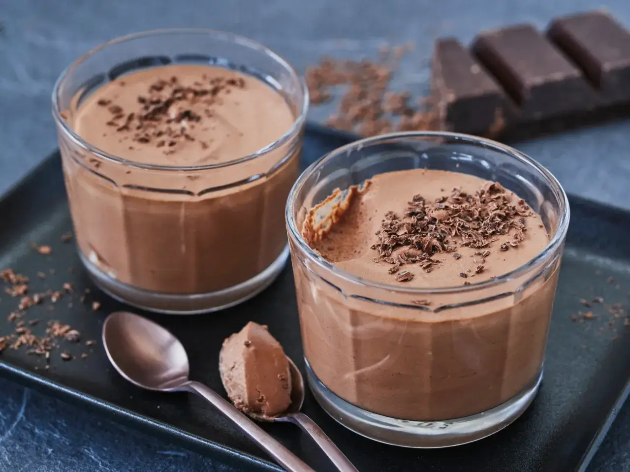 Zwei Gläser mit luftiger Mousse au Chocolat ohne Ei, garniert mit Schokostreuseln. Ein Löffel zeigt die cremige Konsistenz.