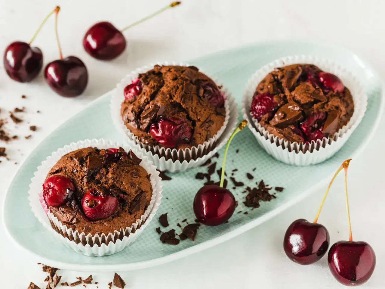 Drei schoko kirsch muffins auf einem Teller, garniert mit frischen Kirschen und Schokoladenst&uuml;ckchen.