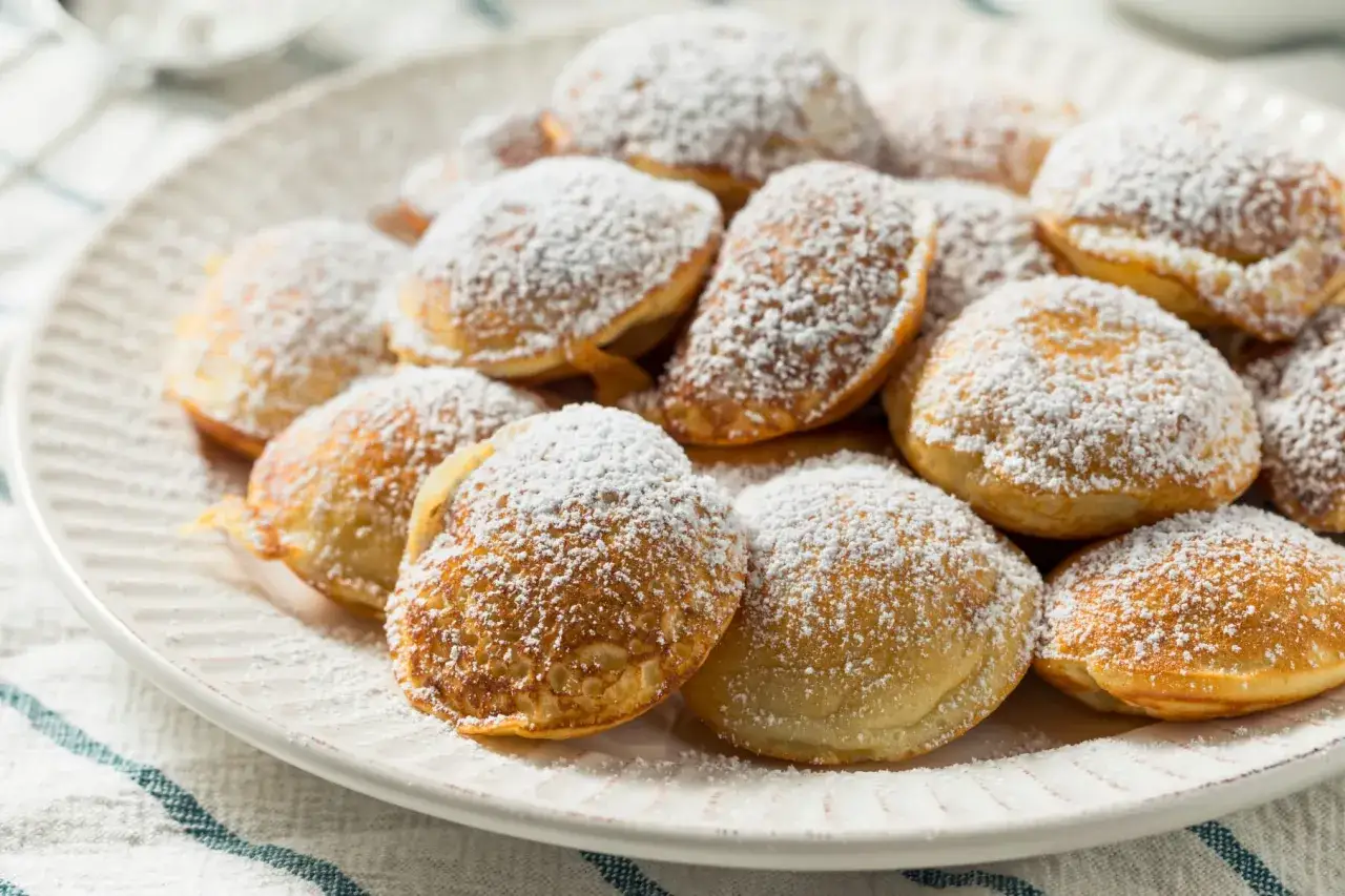 Ein Teller voller goldbrauner Poffertjes, bestäubt mit Puderzucker. Dieses Poffertjes Rezept ist ein Genuss!