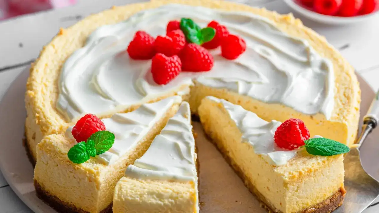 Ein New York Cheesecake, dekoriert mit frischen Himbeeren und Minze, wartet darauf, genossen zu werden.