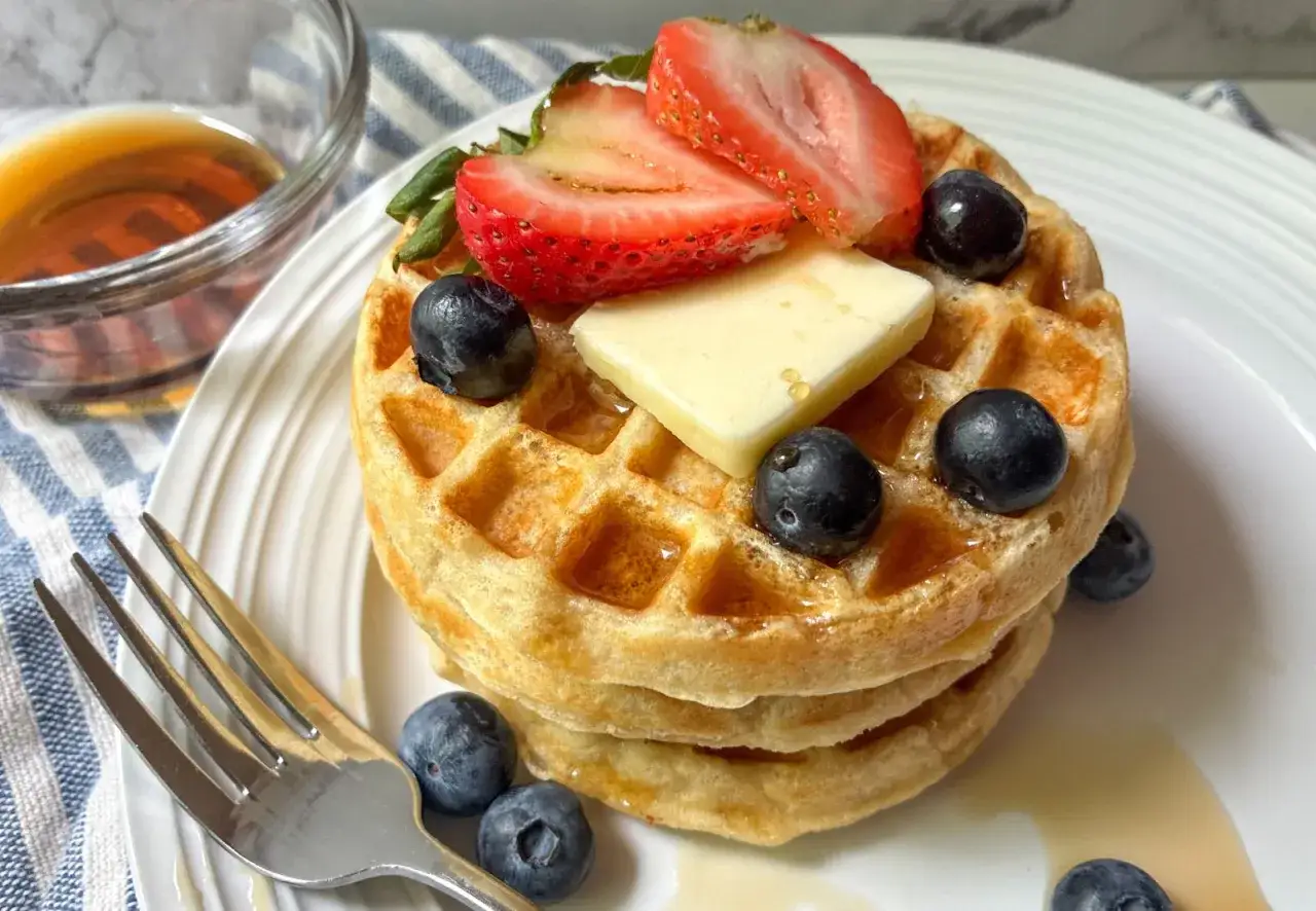 Gestapelte, goldbraune Waffeln ohne Ei, garniert mit Butter, Erdbeeren und Blaubeeren, serviert mit Ahornsirup.