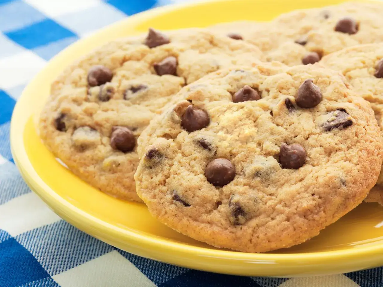 Ein Teller mit frisch gebackenen, goldbraunen Schoko Cookies, die auf einer gelben Unterlage liegen.